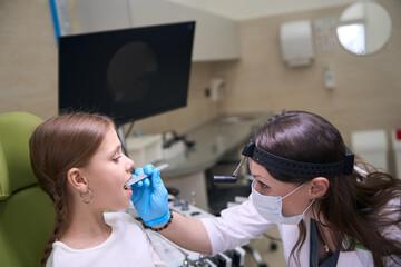 Specialist otolaryngologist in protective gloves examines the childs throat