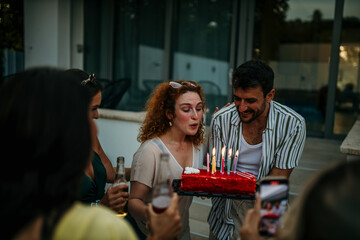 The birthday celebrant makes a wish and blows out the candles, surrounded by cheering friends.