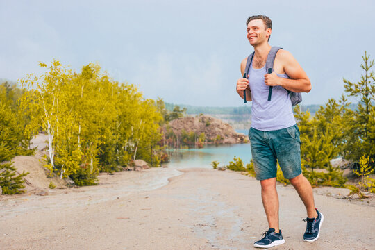 Young handsome man traveler or tourist with backpack hiking in mountains near blue lake with beautiful summer landscape on background. Adventure, travel, holiday concept.