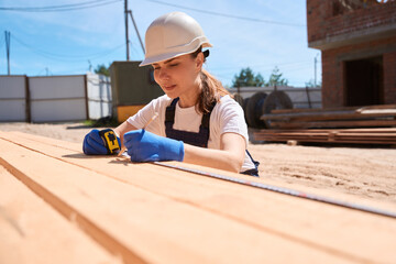 Focused woman carpenter taking measures of wooden beam