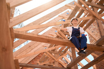 Woman roofer holding hammer, resting from ceiling work, sitting on roof girder