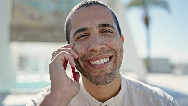 Young hispanic man speaking on the phone at street