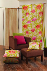 Flowery curtains and cushions on armchair and stool, in green and brown tones, lifestyle