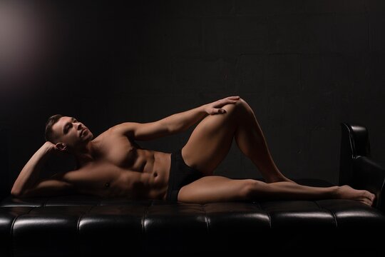 Young muscle man in underwear lying on sofa in dark room