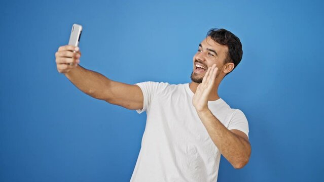 Young hispanic man smiling confident making selfie by the smartphone over isolated blue background