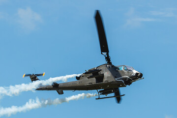 Naklejka na ściany i meble Cobra attack helicopter in flight against blue sky with smoke trailing from pods