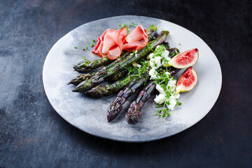 Traditional glazed purple asparagus with prosciutto ham, feta cheese and figs served as close-up on...