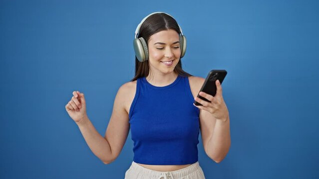 Young beautiful hispanic woman listening to music and dancing over isolated blue background