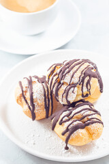 Profiteroles with whipped cream and chocolate filling, with cup of coffee, vertical
