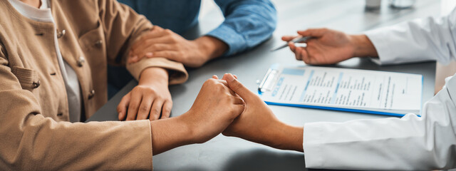 Doctor providing compassionate healthcare consultation while young couple patient holding hand,...
