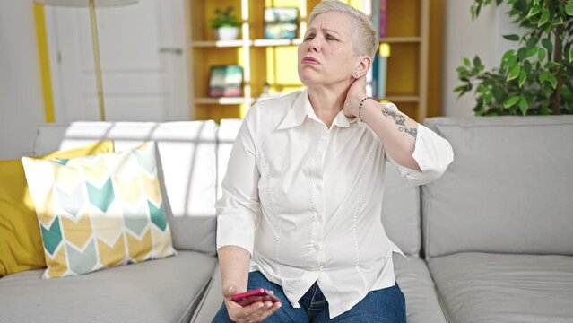 Middle age grey-haired woman using smartphone suffering for cervical pain at home