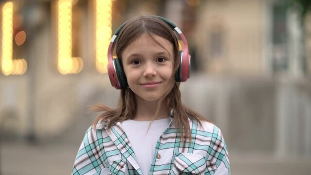 girl puts headphones on her head and listens to music while looking at the camera.