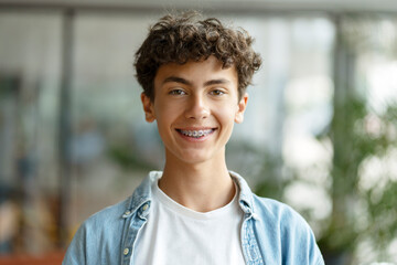 Closeup portrait of smiling smart curly haired school boy wearing braces on teeth looking at...