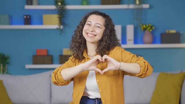 Young woman making heart sign at camera.