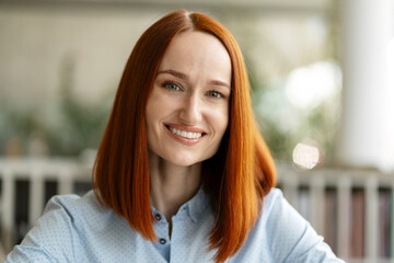Fototapeta premium Closeup portrait of beautiful smiling red haired student standing in university campus, education concept. Confident businesswoman, successful manager looking at camera sitting in modern office 