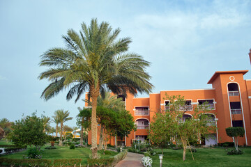 Fototapeta premium Fragment of red brick resort hotel exterior with palm trees under blue summer sky