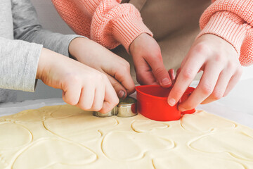 Two caucasian girls cut out shortbread dough with metal and plastic heart shapes.