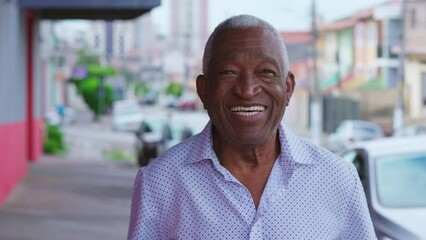 Portrait of a happy black senior Brazilian man standing in street sidewalk looking at camera with smiling expression. Elderly African American male with joyful emotion in urban setting