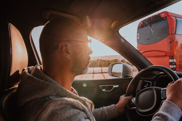 A man with a sunglasses driving a car at sunset. The concept of car travel