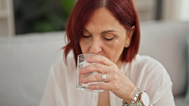 Middle age woman taking pill drinking glass of water at home