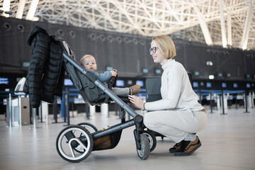 Motherat interacting with her infant baby boy child in stroller while travelling at airport...