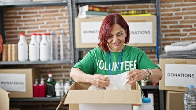 Middle age woman volunteer packing clothes package to donate at charity center