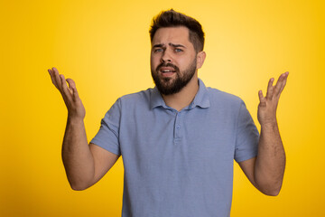 What Why. Sincere irritated caucasian man raising hands in indignant expression asking reason of failure demonstrating disbelief irritation by trouble. Handsome confused guy on yellow background