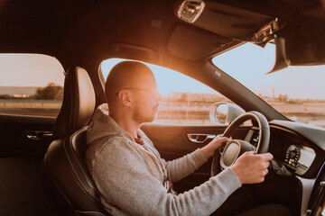 Fototapeta premium A man with a sunglasses driving a car at sunset. The concept of car travel