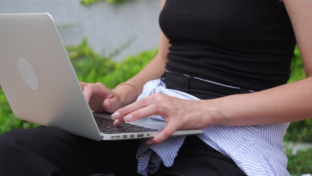 young attractive smiling brunette girl freelancer working at her laptop outside in the park. close-up