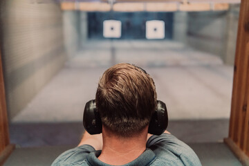 A man practices shooting a pistol in a shooting range while wearing protective headphones