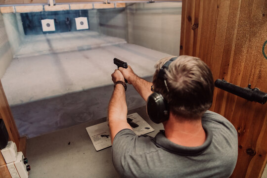 A man practices shooting a pistol in a shooting range while wearing protective headphones
