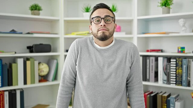 Hispanic man student standing with i dont know expression at library university