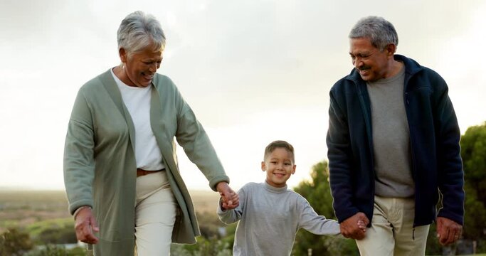 Grandparents walking and holding hands with their grandchild in nature on family holiday. Happy, smile and senior man and woman in retirement bonding with boy kid on outdoor weekend trip or vacation.