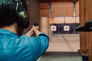 A man practices shooting a pistol in a shooting range while wearing protective headphones