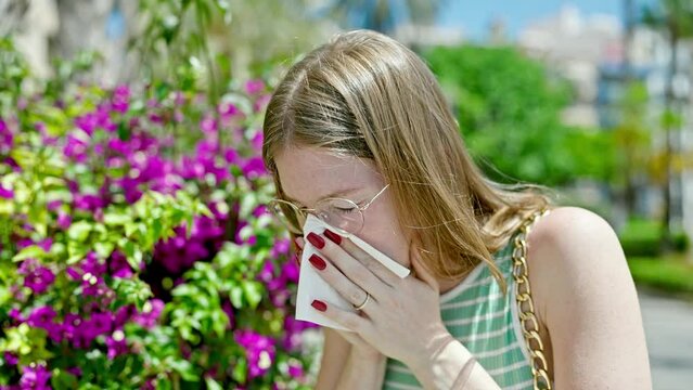 Young blonde woman sneezing for allergy at park