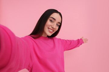 Smiling young woman taking selfie on pink background, space for text - obrazy, fototapety, plakaty