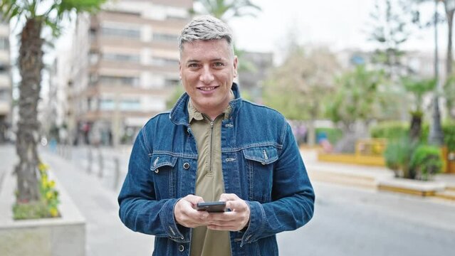 Young caucasian man using smartphone smiling at street