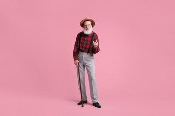 Fototapeta premium Senior man with walking cane showing his tongue and rock gesture on pink background