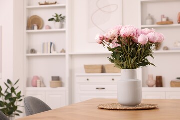 Vase with pink peonies on wooden table in dining room. Space for text