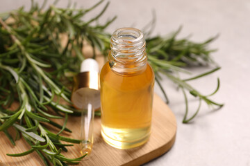 Bottle of essential oil and fresh rosemary on light grey table, closeup