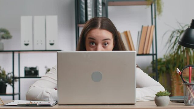 Caucasian business woman hiding behind laptop computer making funny face, fooling around, putting his tongue out remote working disrespecting someone at office workplace. Professional freelancer girl