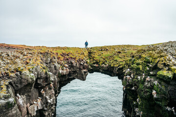 Man standing on rock arch natural bride in Arnarstapi in Iceland