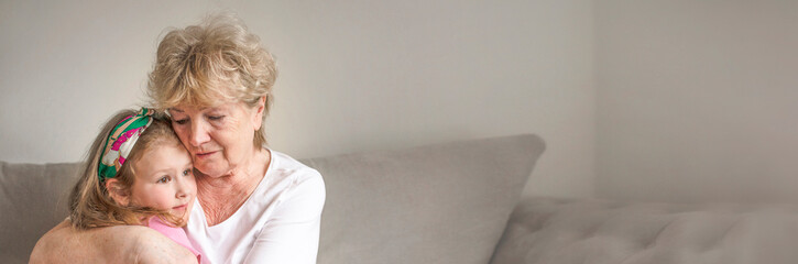 Grandmother hugging grand kid on couch at home, holding little girl in arms. senior grandma...