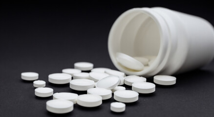 white jar with watered pills on black background. pills and medicine concept