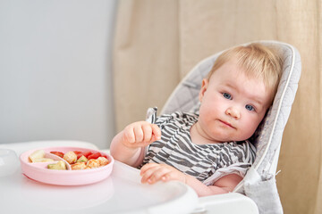 Cute child eats healthy food vegetables and meatballs from dietary meat steamed,. Portraits of a cute 10 months old baby girl. The baby sitting in a special high chair for babies.