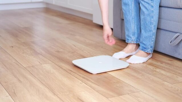 Woman in blue jeans weighing herself on floor scales