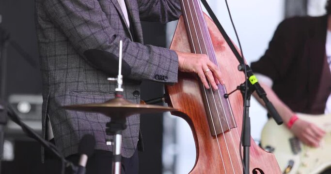 Concert view of a contrabass violoncello player with vocalist and musical rock band during jazz orchestra band performing music, violoncellist cello jazz player on stage 
