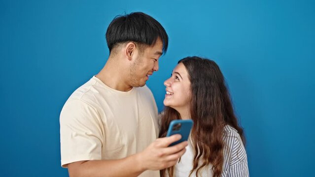 Man and woman couple smiling confident using smartphone over isolated blue background
