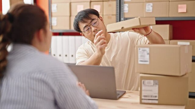 Man and woman ecommerce business workers using laptop holding package at office