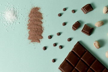 Black chocolate bar, chips, cocoa, pistachios and grated coconut on a turquoise background.